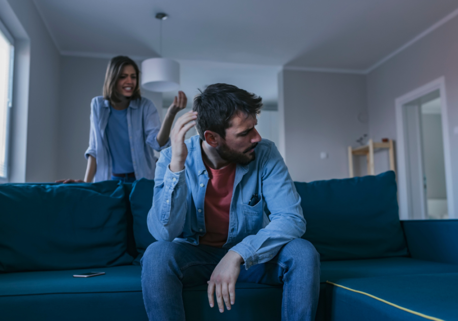 man sitting on the couch and a woman talking behind him signs he never loved you