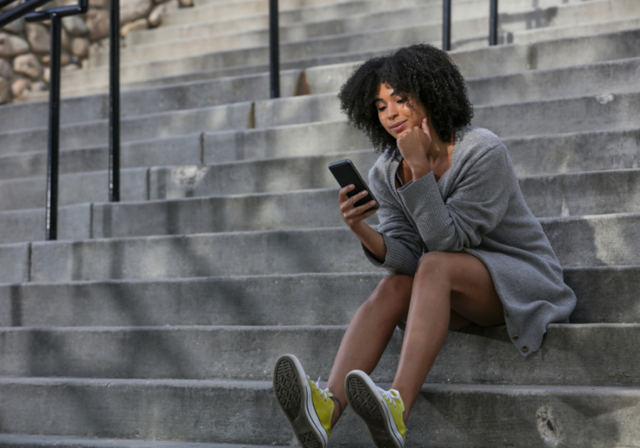 woman sitting on steps looking at phone Hinge 'Dating Me Is Like' Prompt