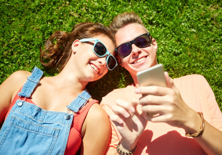 couple laying on grass looking at phone dating apps for teenagers