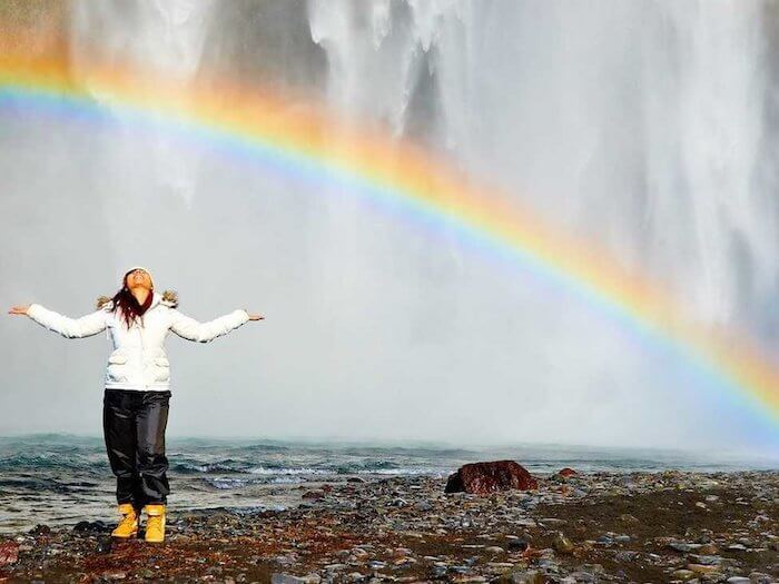 woman beside beach with rainbow benefits of positive thinking