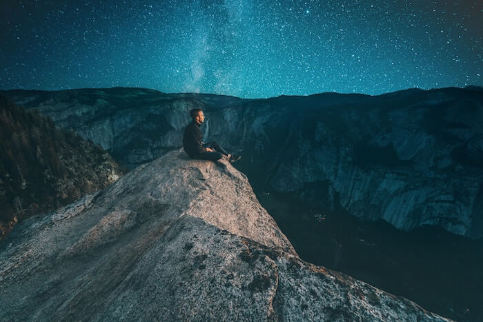 man sitting on mountain peak at dark things to be passionate about