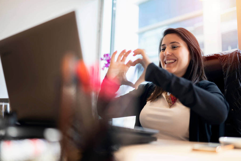 woman at office video chatting while making heart shape with her hands