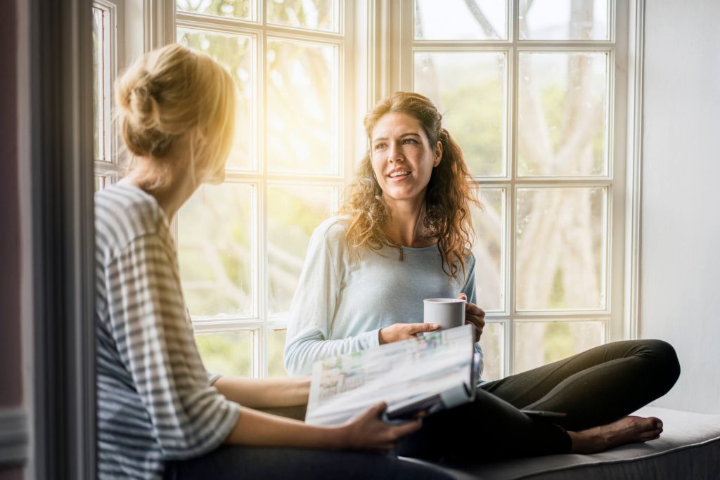 women sitting beside window talking questions to ask your sister