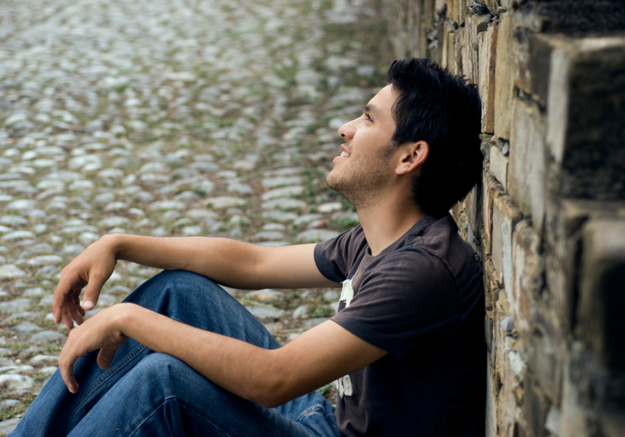 man smiling sitting on the sidewalk signs your twin flame is communicating with you