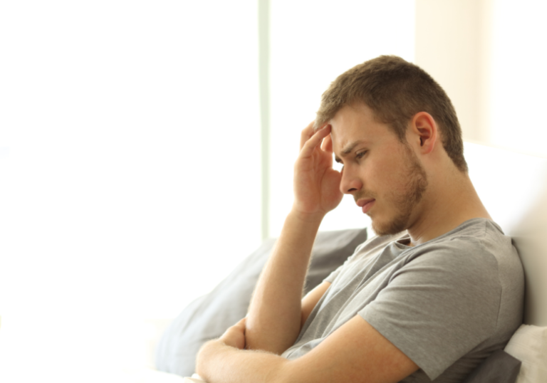 man holding his head while sitting in couch signs of a weak man in a relationship