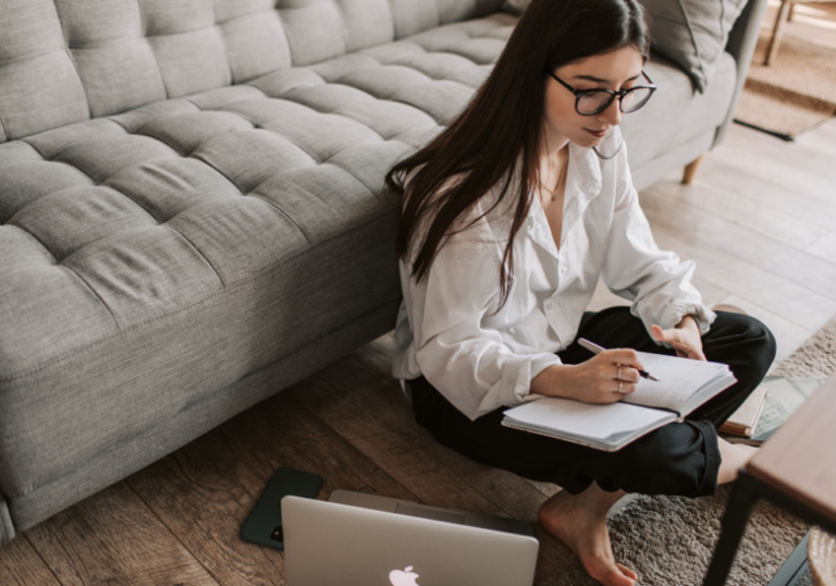 woman with laptop and writing in notebook while sitting on the floor