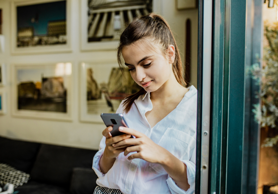 woman standing by the window using phone deep things to say to your boyfriend over text