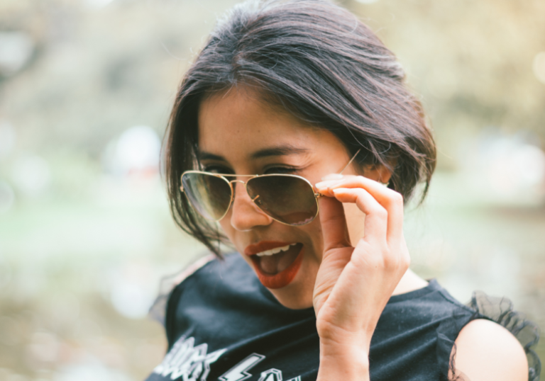 woman holding her shades winking playfully how to know if a girl is playing you