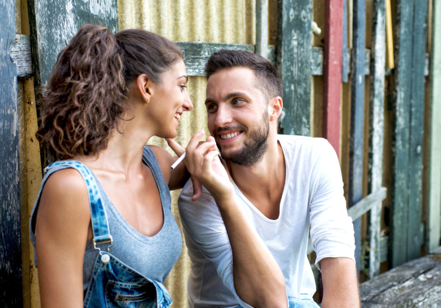 man holding a cigarette while touching a woman's face leading someone on