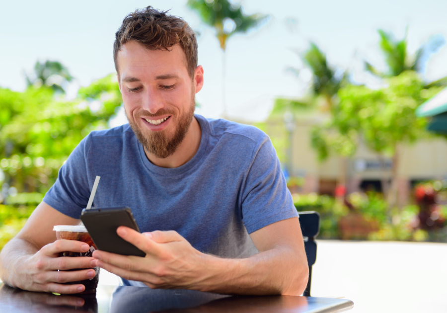 man with iced coffee smiling while looking at phone good morning text to your crush