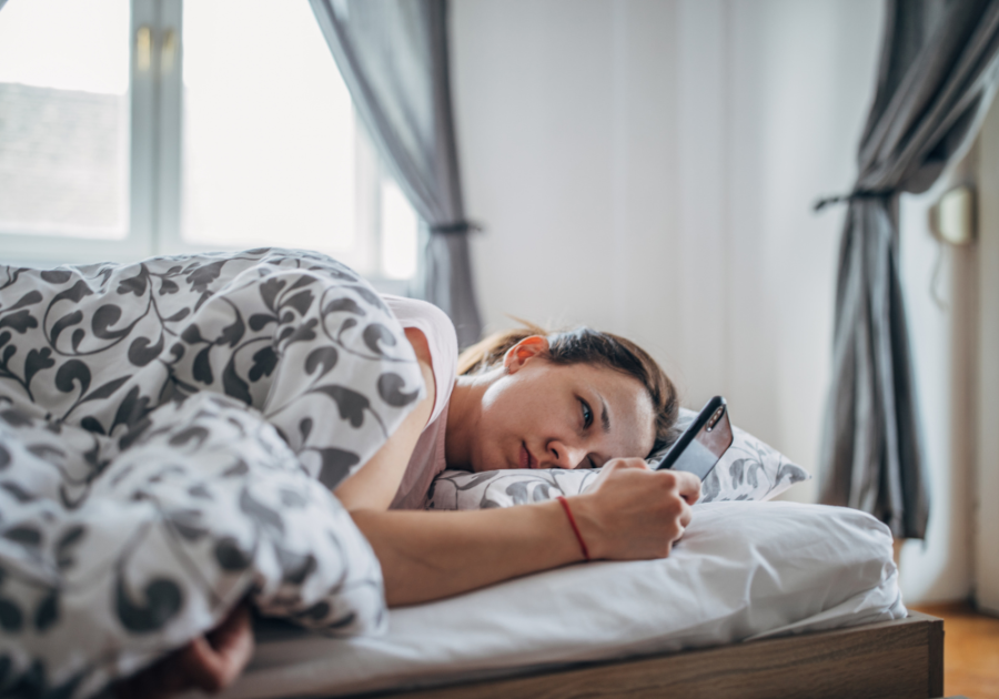 woman lying in bed looking at phone Why is he ignoring me all of a sudden