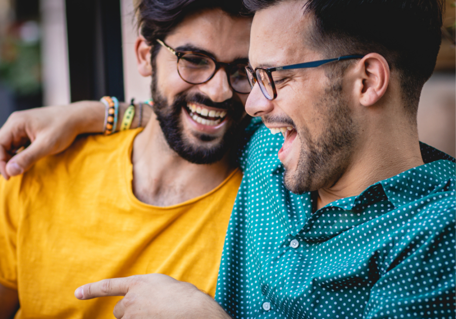 two men laughing sitting with arm around him Signs of Bisexuality in Males 