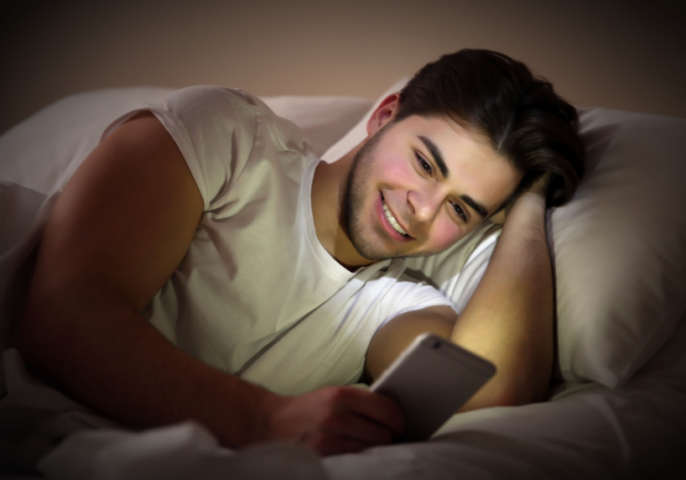 young man laying in bed looking at phone Hot Romantic Goodnight Quotes