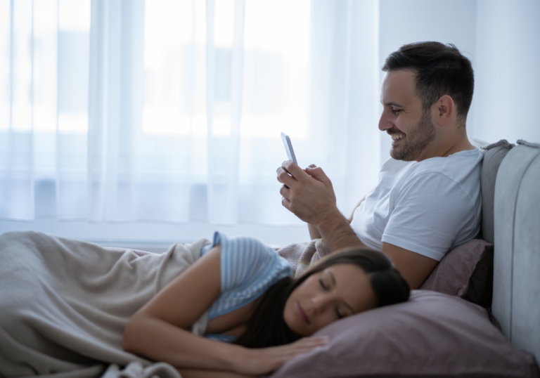 couple in bed man is looking at phone is secting cheating